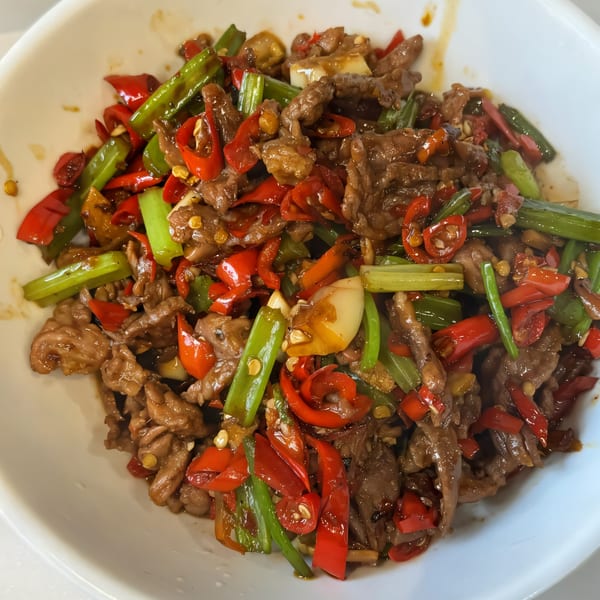 Chef Wang's spicy stir-fried beef with red chili peppers and green vegetables in a white bowl.