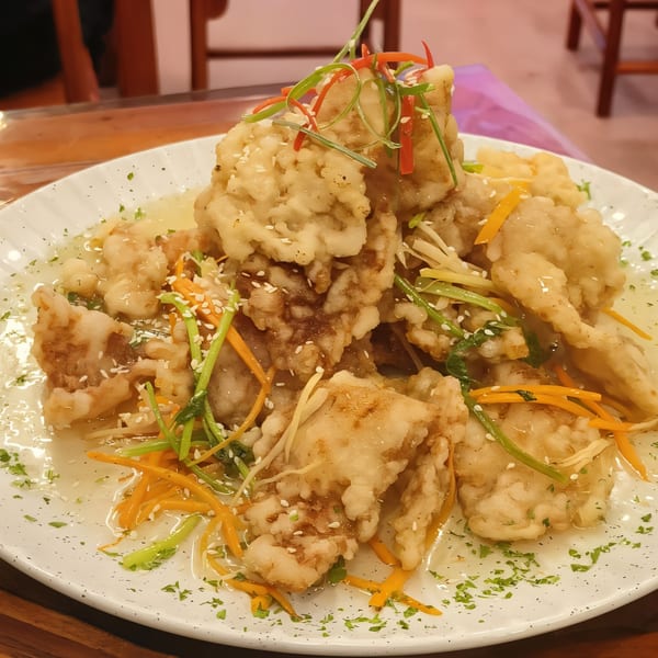 Crispy fried fish with sweet and sour sauce, garnished with carrots, scallions, and sesame seeds.