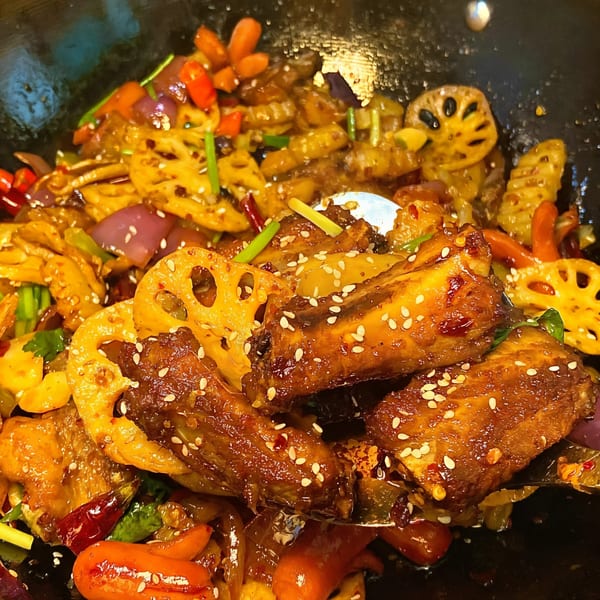 Chef Wang's Chinese stir-fry with chicken wings, lotus root, and vegetables in a dark pan.