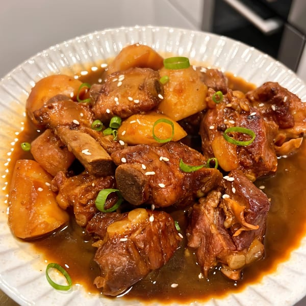 Braised pork ribs and potatoes in a rich brown sauce, garnished with sesame seeds and green onions.