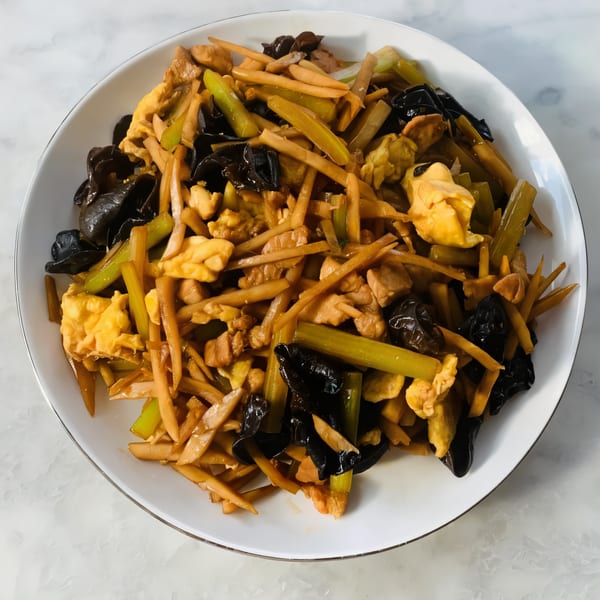 A white plate filled with stir-fried bamboo shoots, wood ear mushrooms, scrambled eggs, and chicken.